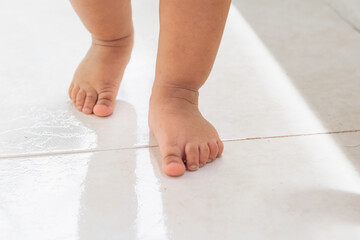 close-up of the feet of a latin baby girl taking her first steps, standing on a white background