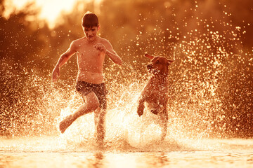 Boy running with dog at beach at summer sunset