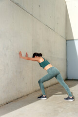 woman doing a calf or leg stretch against a  concrete wall outside, warm up exercises. © Rob Wilkinson