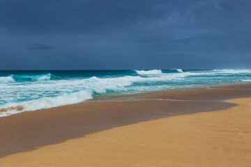 Tropical beach on an overcast day with turquoise waves crashing onto sandy shore
