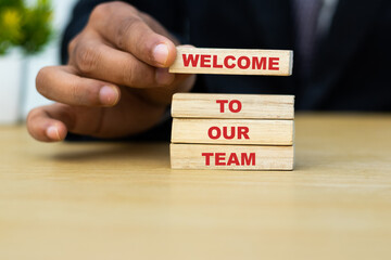 Welcome to our team word on wooden block hold by businessman hand