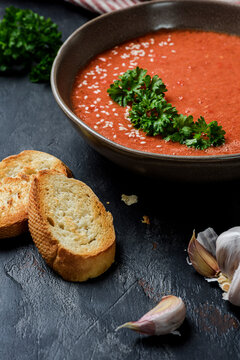 Gazpacho garnished with parsley in a plate with wavy edges. There is garlic and  croutons on the table.