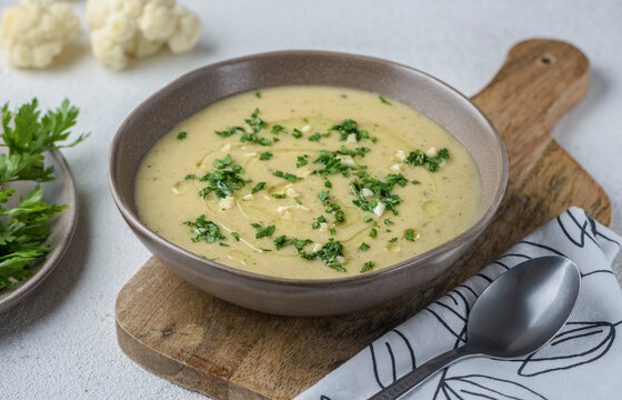 White vegetable cream soup. The dish is seasoned with parsley and garlic. There is a spoon and a napkin nearby.