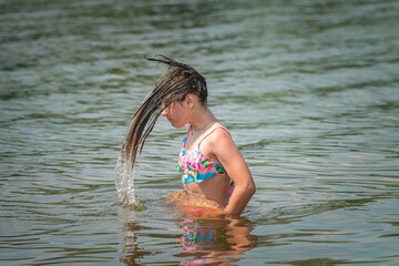 A beautiful little girl plays swimming in the river.