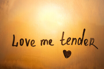 Handwritten text love me tender written finger with heart shape on orange sunset frozen window - Powered by Adobe