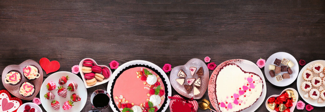 Valentines Day bottom border of assorted desserts and sweets. Top view over a dark wood background. Love and hearts theme. Copy space.
