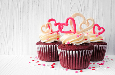 Valentines Day theme red velvet cupcakes with sweet hearts and white icing. Side view with a white...