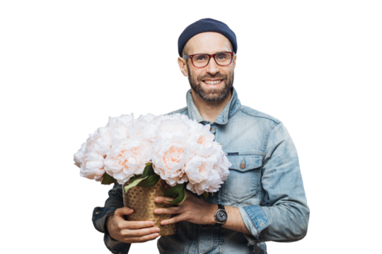 Satisfied bearded male with cheerful expression has broad smile, holds bunch of flowers, wears hat and denim jacket, isolated over white background. Satisfied smiling man poses indoor with flowers - Powered by Adobe