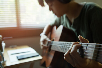 Enjoy a young Asian musician holding an acoustic-electric playing guitar and singing song at home