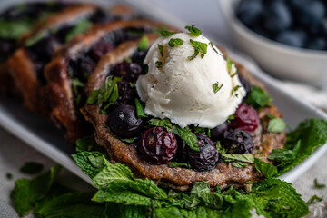 Blueberry tart on chocolate puff pastry; garnished with mint and a scoop of vanilla ice cream.