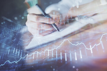 Financial forex graph displayed on hands taking notes background. Concept of research. Double exposure