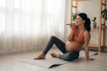 Fototapeta na wymiar Pregnant woman talking on the smart phone and resting on a mat after workout at home.