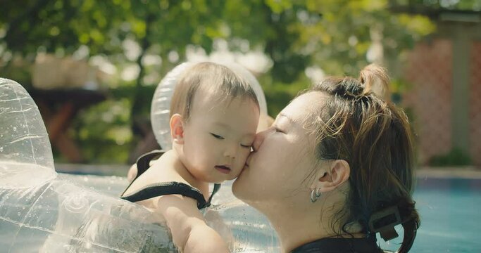 Happiness Asian family mother playing water with cute adorable baby toddler daughter girl having fun together in swimming pool, mom kissing little kid with love in vacation holiday summertime