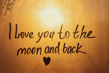 Handwritten text I love you to the moon and back written finger with heart shape on orange sunset frozen window