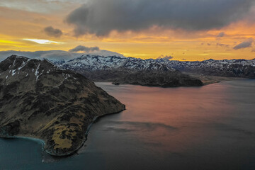 Aerial view of a mountain range with snow on the crests along the Dutch Harbour on Amaknak Island at sunset, Unalaska, Alaska, United States.