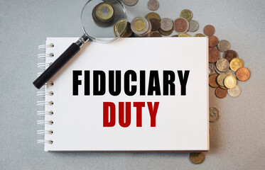 Notepad with the inscription FIDUCIARY DUTY. Conceptual image, a notepad along with coinlets and a magnifying glass on a desktop. Finance or business concept.