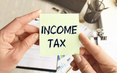 INCOME TAX written on a voucher shown by a female businessman. Soft focus.