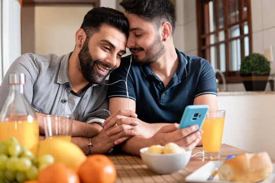 Romantic Gay Couple Using Mobile Phone And Watching Video Together At Home