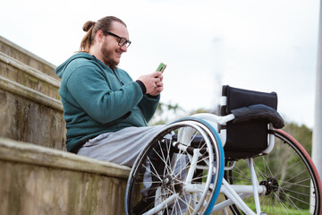 person in wheelchair using mobile phone and smiling in basketball court outdoor