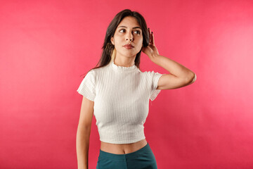 Beautiful brunette woman wearing white ribbed crop isolated over red background bewildered,...