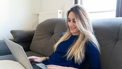 Young caucasian woman using laptop at home. Blonde woman smiling and shopping online.