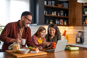 Cheerful young family preparing meal in the kitchen, participating in an online cooking class.