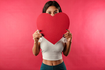 Portrait of young brown-haired woman wearing ribbed crop isolated over red background covering...