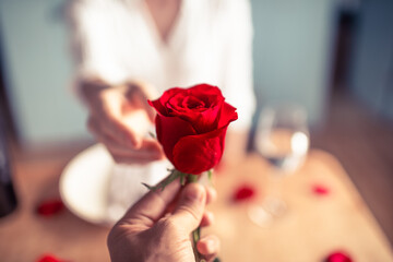 Man giving woman a single red rose in a romantic dinner date night setting. 