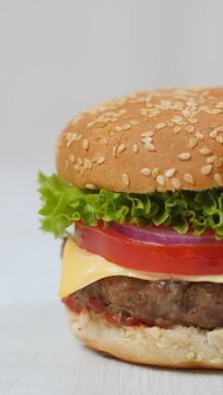 Vertical video. Half of a burger sandwich is visible on a light wooden background. Camera movement - vertical panorama.