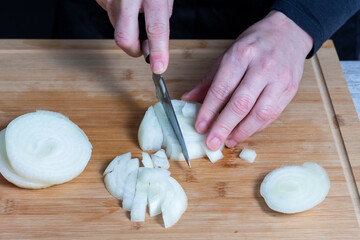 Slightly blurred working woman's hands using a knife to cut onion on a wooden kitchen board. Food preparation concept.