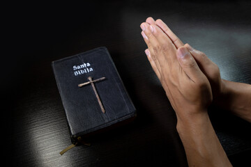 Mano en posición de orar o rezar y sosteniendo la santa biblia y cruza de clavos envuelto con un...