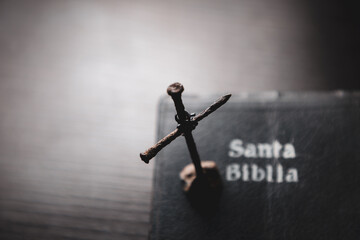 Portada de santa biblia en una meza y clavos oxidados formando una cruz encima del escritorio de pintura negra y destellos de luz.