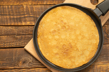 Thin pancake in a frying pan, on a wooden background, freshly cooked, top view, space for text.