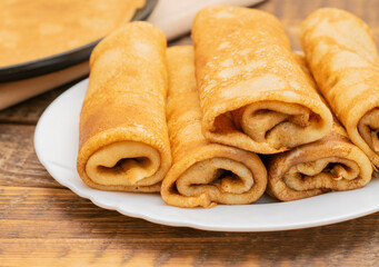 Thin pancakes rolled up on a white plate close-up. Traditional Russian, Ukrainian pancakes on milk with filling.