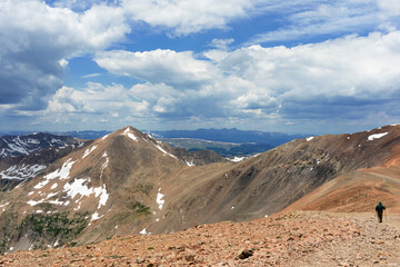 Mount Democrat at 14,155 elevation as seen from the saddle between Mount Bross and Mount Cameron with blue sky and cumulus clouds with a single hiker