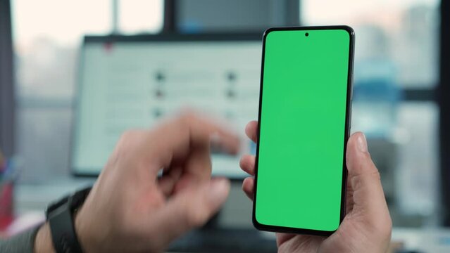 Close Up of Smartphone with Green Screen Mock Up Display In Male Hands. Man Sitting In Office Browsing Internet , Watching Content, News, Financial Reports on Phone