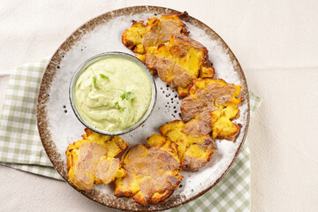 Trendy comfort snack crispy roasted crushed potatoes on a round plate with creamy avocado and garlic dip on a green checkered kitchen towel