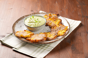Trendy comfort snack crispy roasted crushed potatoes on a round plate with creamy avocado and garlic dip on a green checkered kitchen towel on wooden background