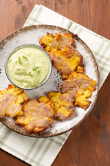 Trendy comfort snack crispy roasted crushed potatoes on a round plate with creamy avocado and garlic dip on a green checkered kitchen towel on wooden background, top view
