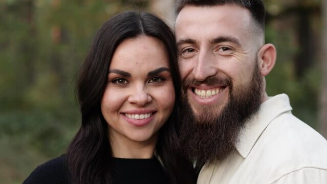 Portrait of happy young woman and man looking in camera enjoy romantic date in park. Smiling bearded man and brunette girl feeling happiness outdoors. Romantic couple enjoying leisure time together
