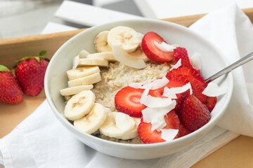 Breakfast oatmeal with fresh banana and strawberries served on wooden kitchen tray