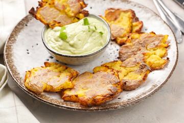 Trendy comfort snack crispy roasted crushed potatoes on a round plate with creamy avocado and garlic dip on a beige colored table cloth