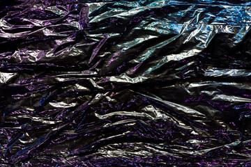 Black color plastic wrap background. Dark crumpled wrinkled plastic cellophane. Reflecting colorful...