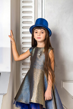 Portrait disco girl model in blue dress and hat posing at bright white cosmic background, looking at camera. Beautiful party girl with long hair in blue wear. Retro music style concept. Copy space