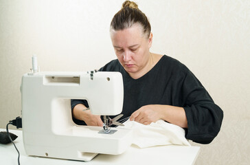 A female seamstress sews white fabric items on a sewing machine.