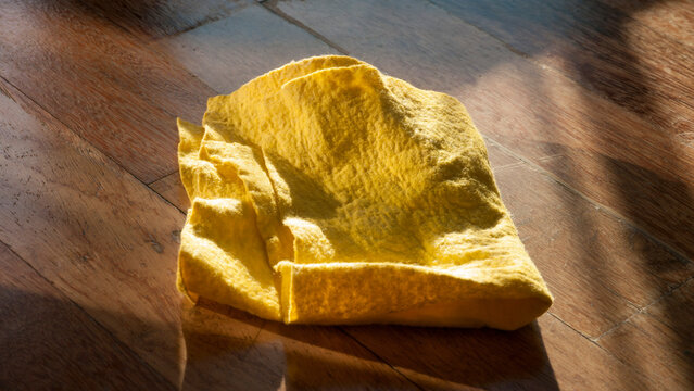 Bayeta de tejido absorbente amarillo sobre suelo de madera