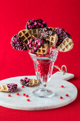 A cinnamon heart filled dessert glass holding decorated Valentine waffle pops.