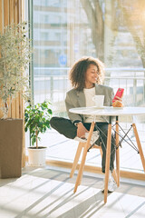 Young smiling african american girl drinking coffee and eating tasty croissant in a cozy cafe. Holidays, lunch time and vacation concept	             