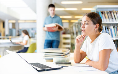 Obraz premium Positive young lady in casual clothes working remotely using a computer in a quiet library