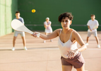 Sporty young Argentinian woman playing traditional team match of pelota at open-air fronton on...